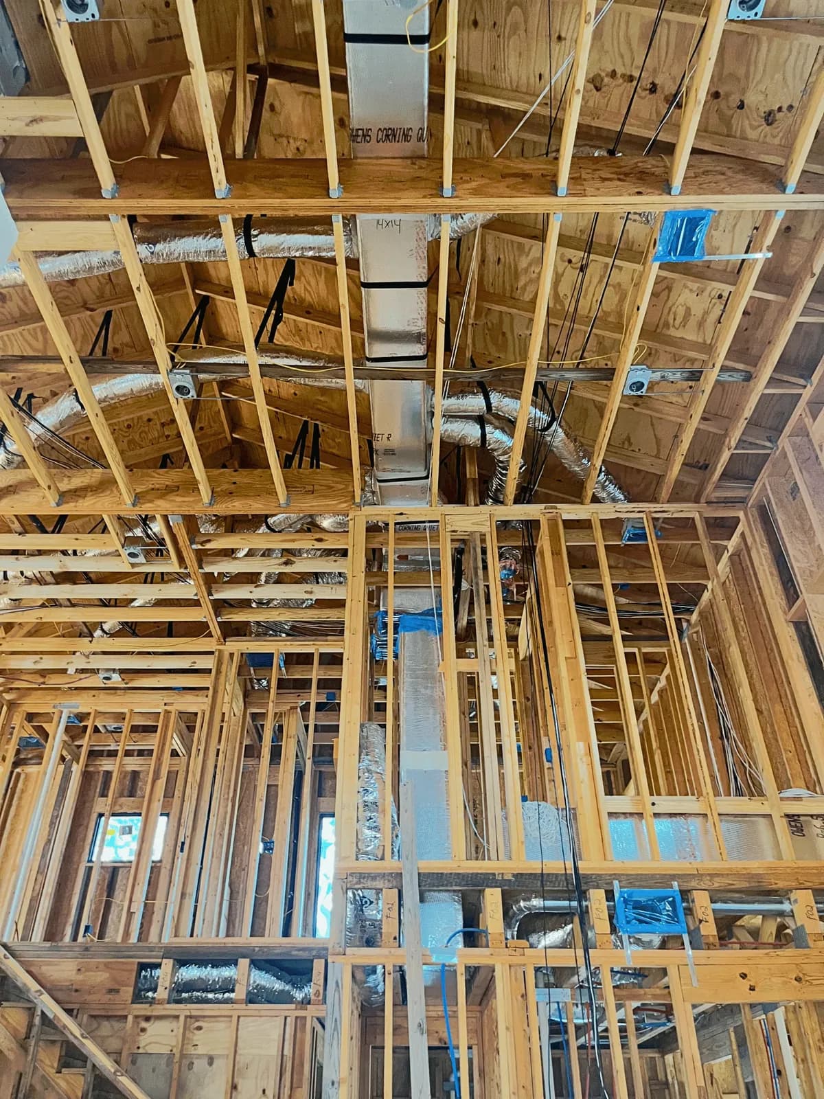 A rectangular duct board trunk marked 14 by 14 running up through vaulted ceiling framing, with insulated flexible branches teed off toward individual rooms.